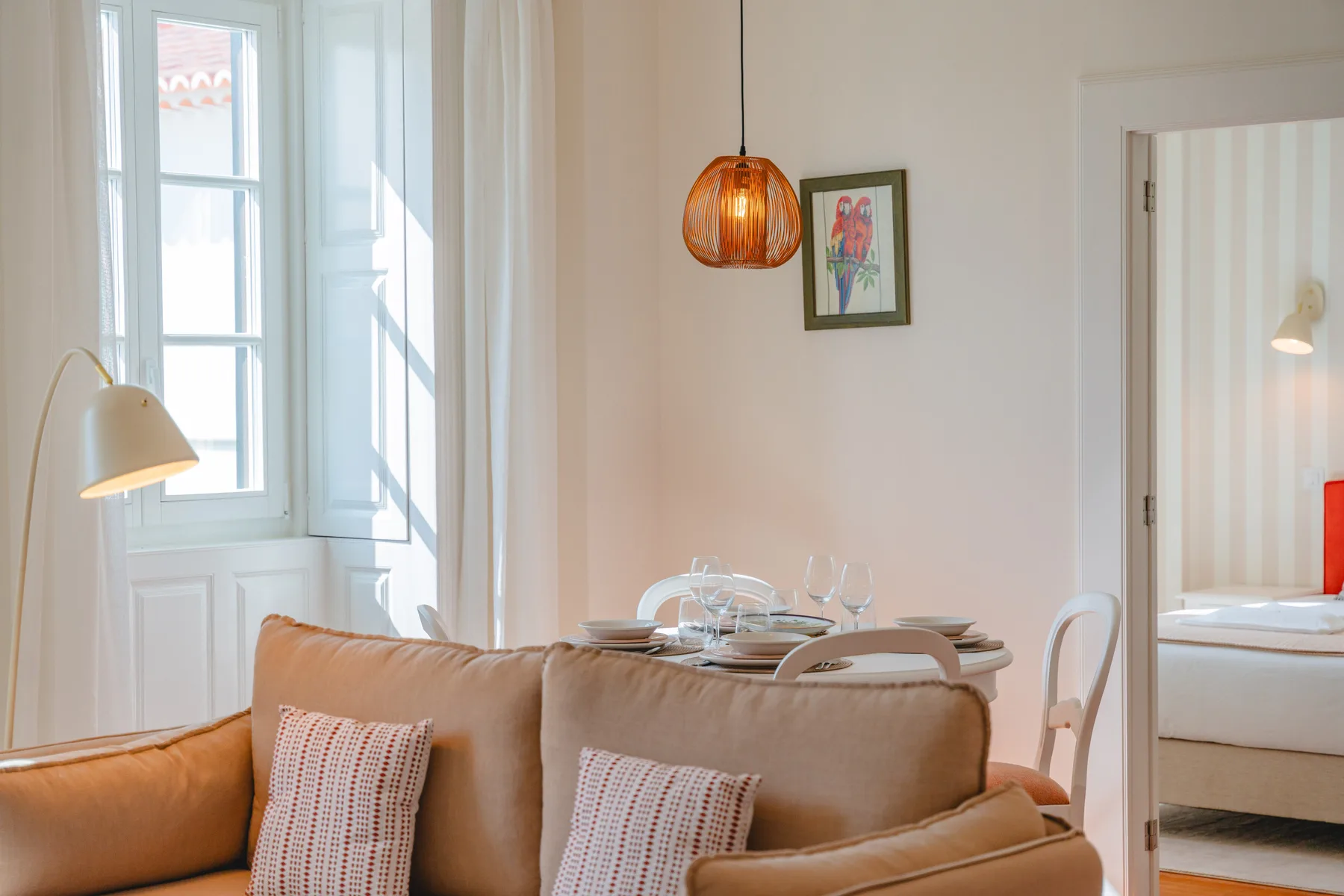 A bright living and dining area with seating, a set table, and tall windows.