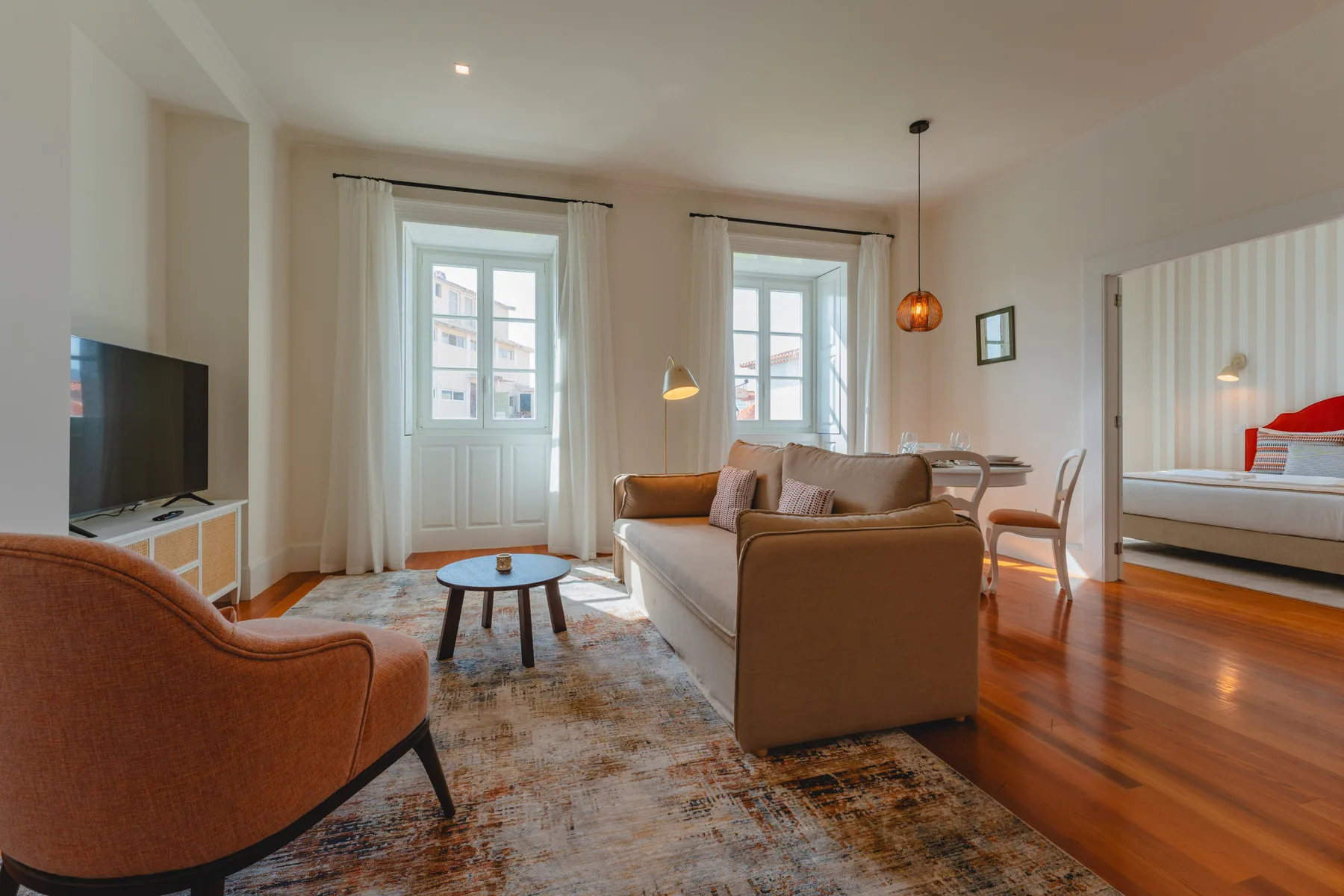 A living room with seating, a television, and tall windows opening onto a balcony.