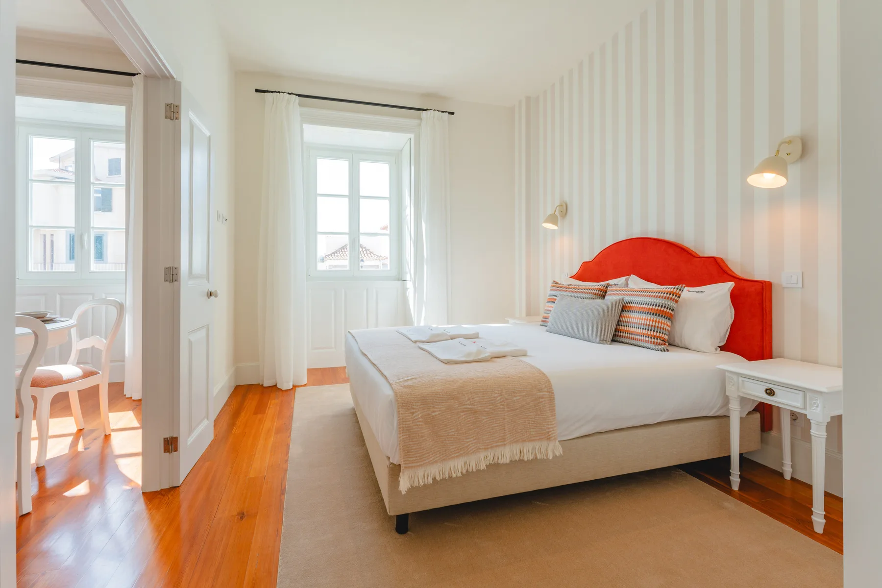 A bright bedroom with a neatly made bed beside a window.