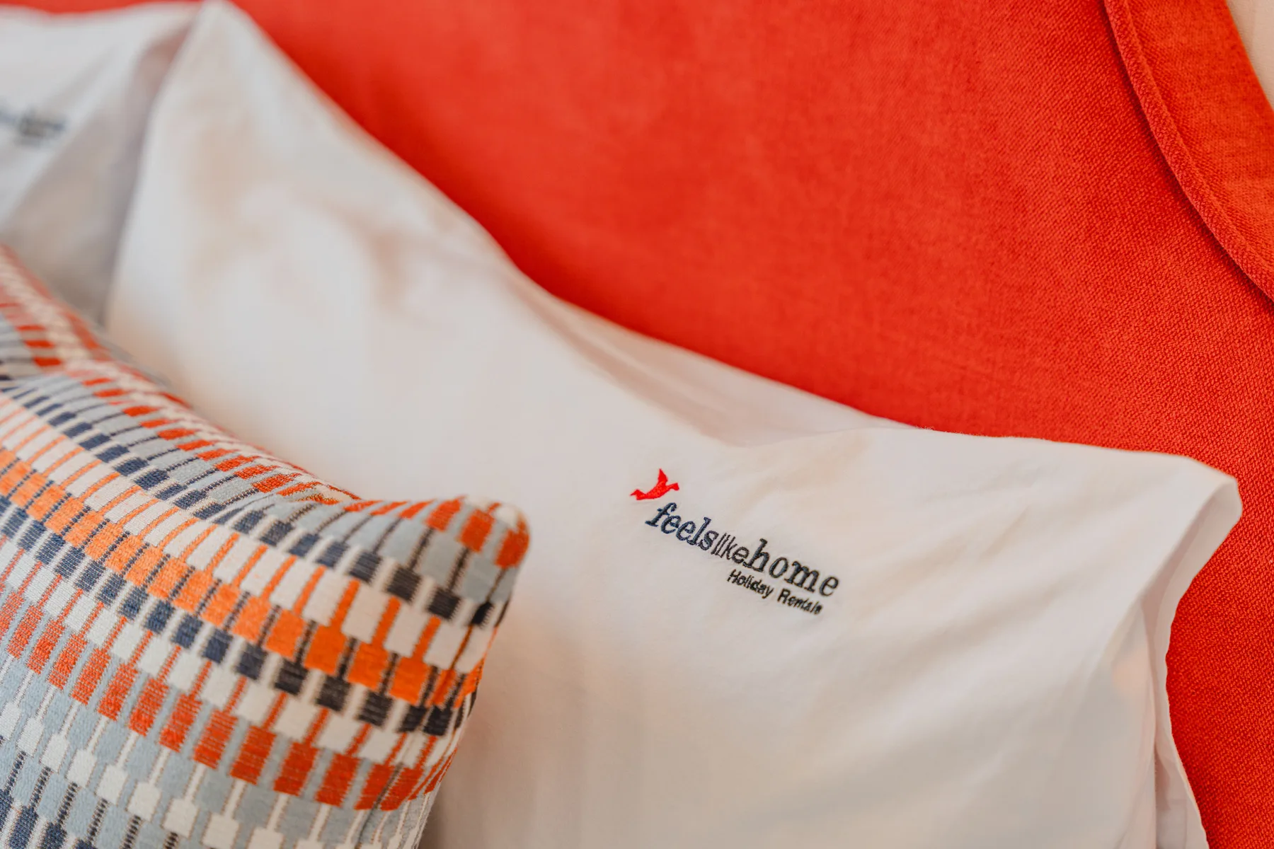 A close-up of white bedding with a patterned cushion against a red headboard.