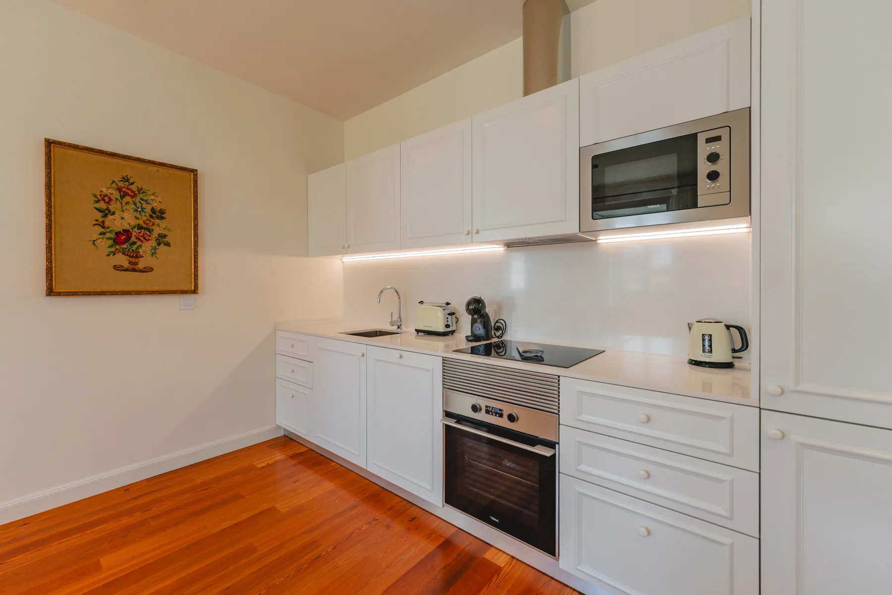 A compact kitchen with white cabinets, a cooktop, and a built-in oven.