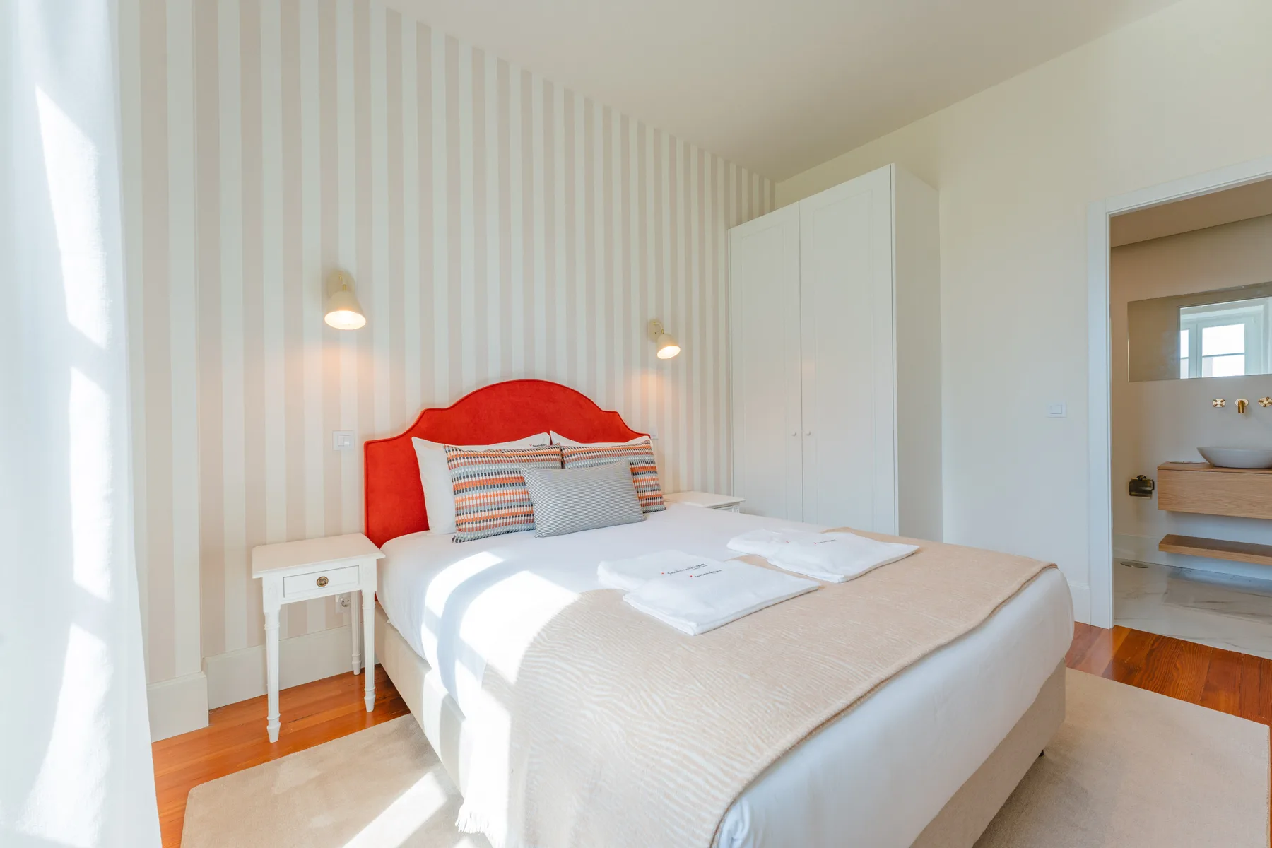 A bright bedroom with a bed, bedside table, and striped walls.