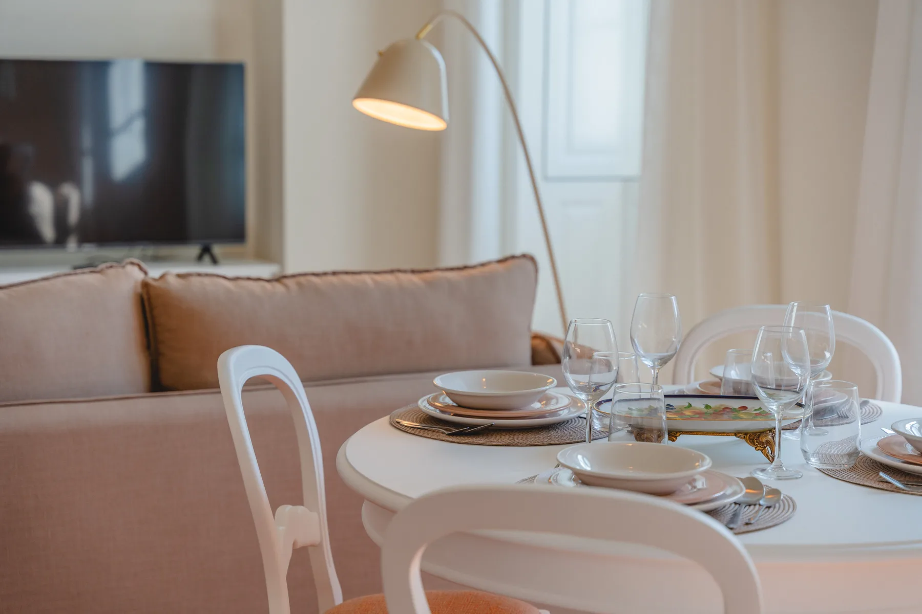 A dining area with a set table beside a sofa and television.