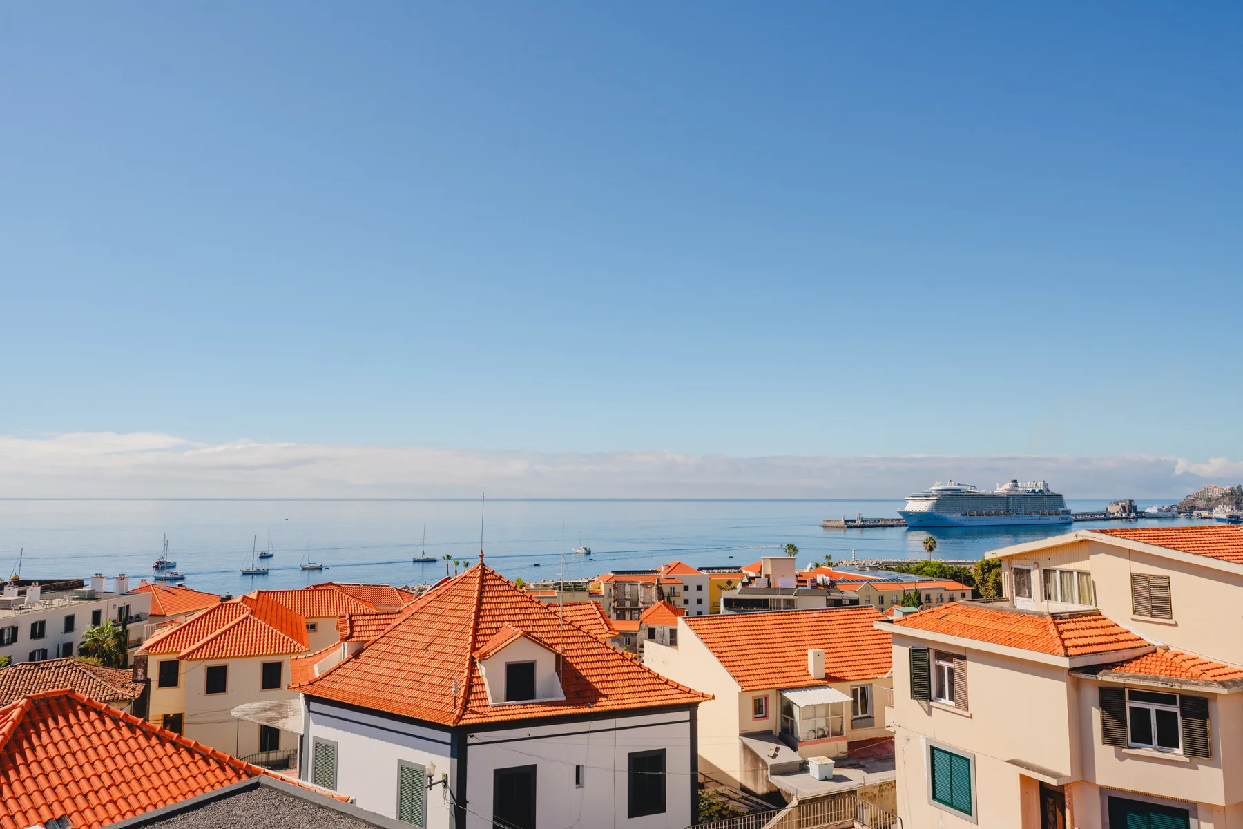A coastal townscape with red-tiled rooftops and the sea in the background.