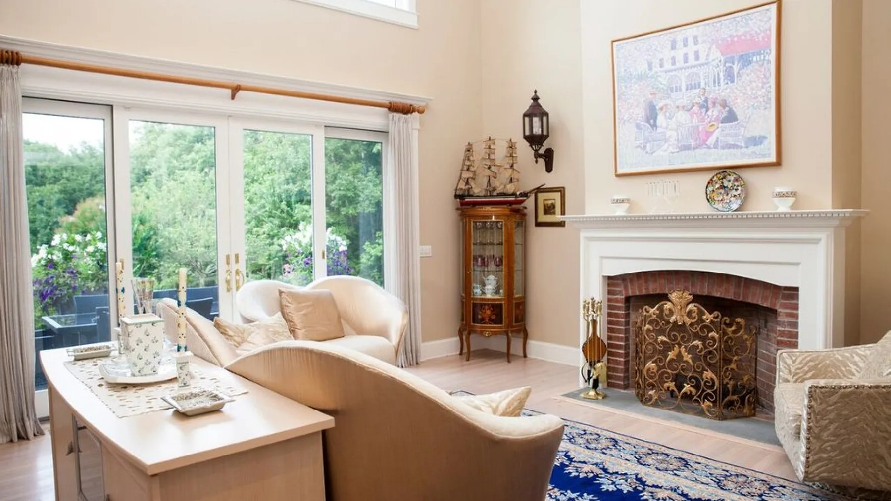 A living room with a fireplace, seating, and large windows overlooking greenery.