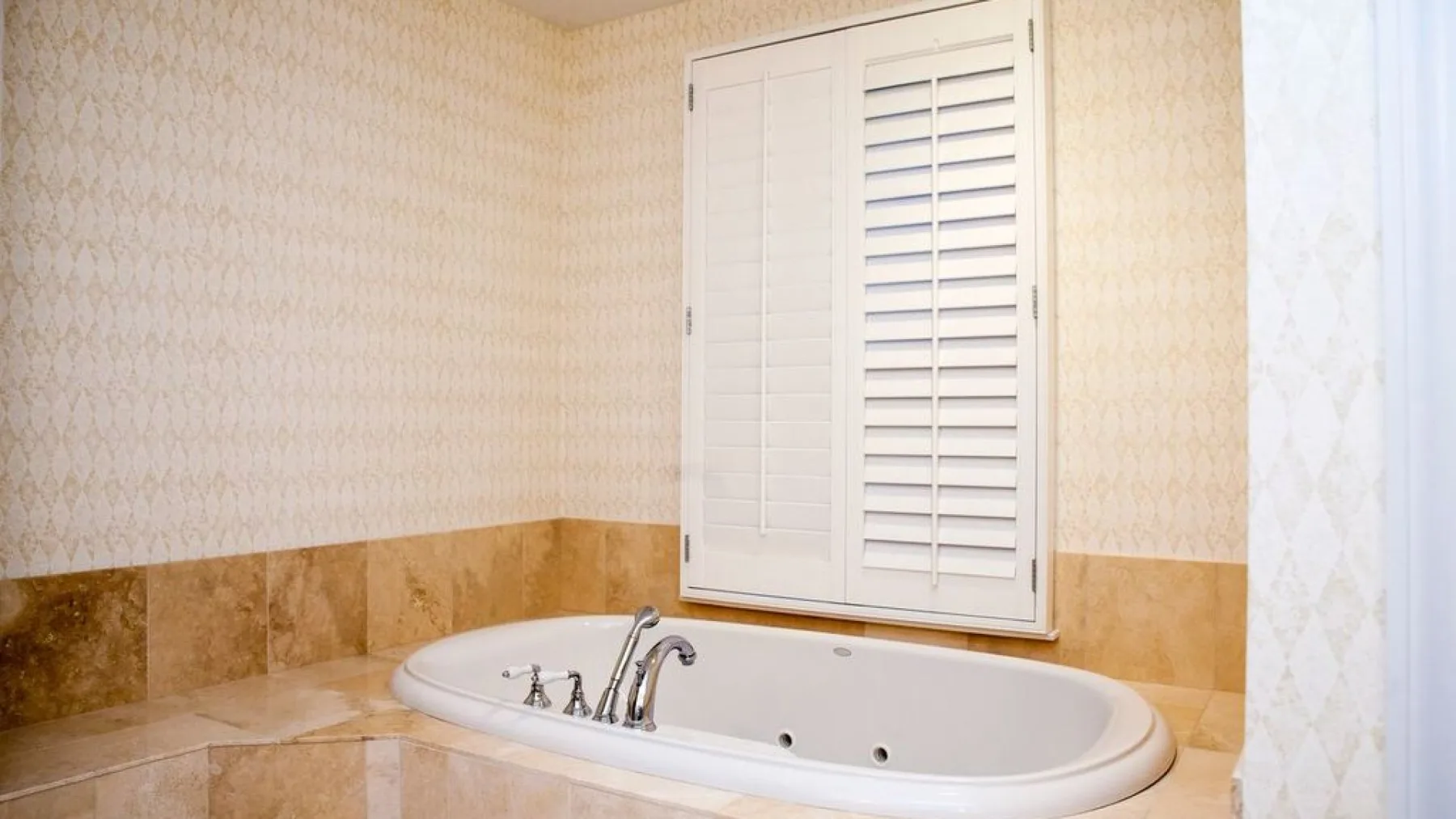 Una bañera de baño está bajo una ventana con contraventanas.