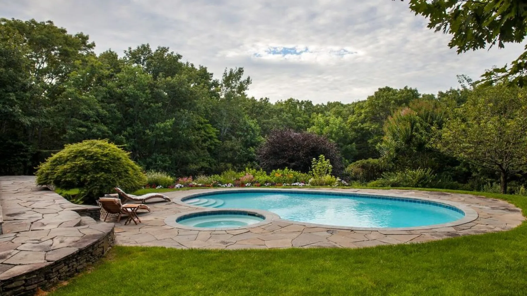 Una zona de piscina al aire libre con un pequeño spa circular y pavimento de piedra.