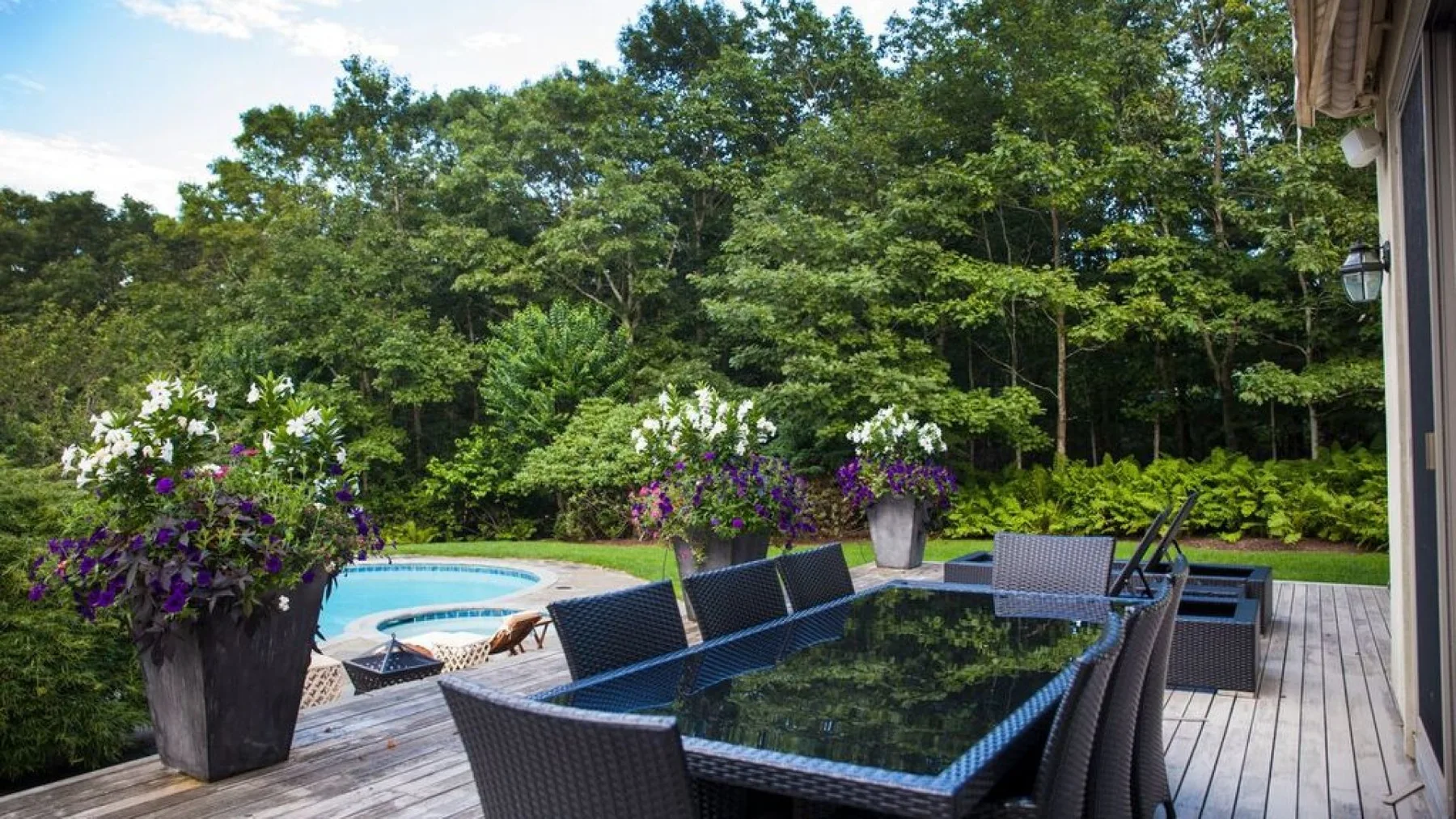 Un patio al aire libre con asientos da a una piscina y una zona arbolada.