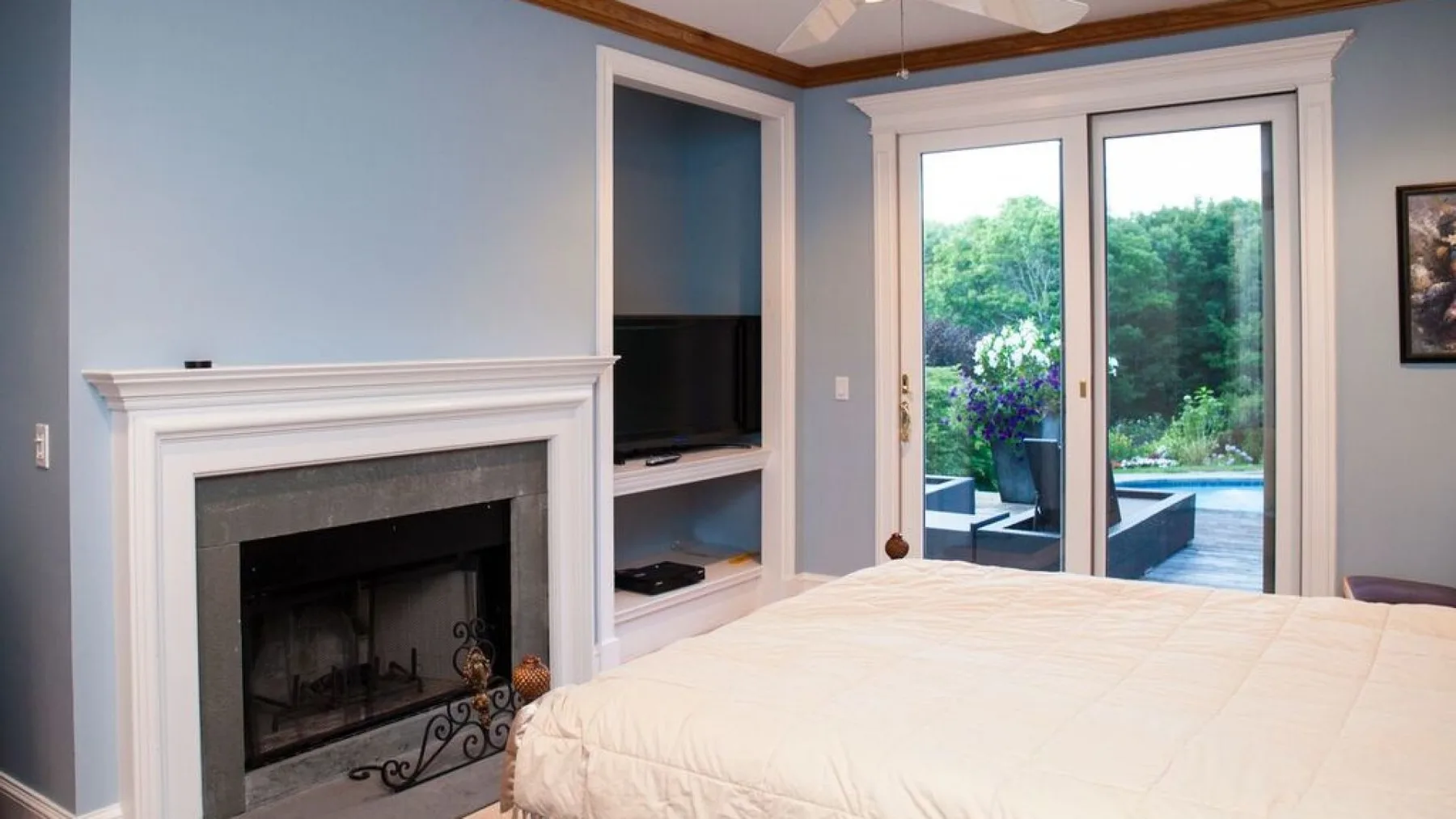 Dormitorio con una cama junto a una chimenea y puertas de vidrio hacia el jardín.
