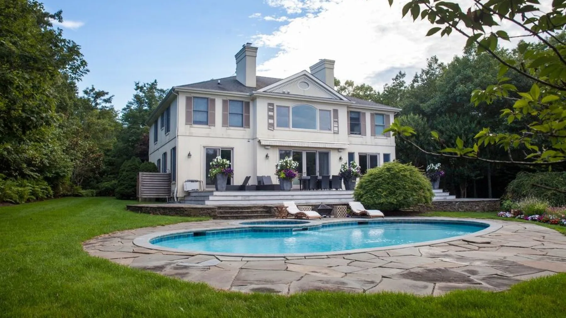 Una casa grande da a una piscina curva y un patio pavimentado.