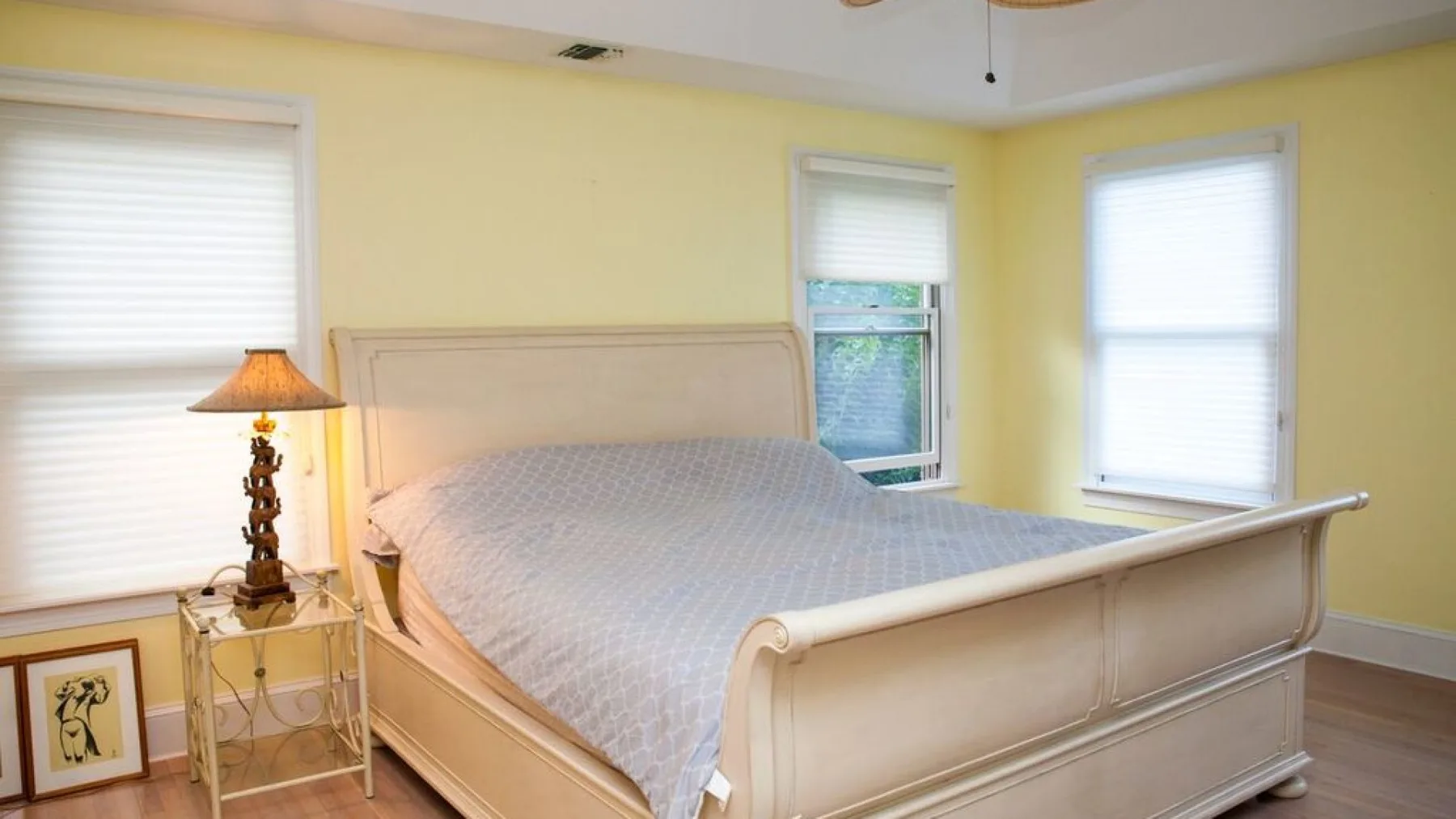 Un dormitorio con una cama grande, paredes amarillo pálido y varias ventanas.