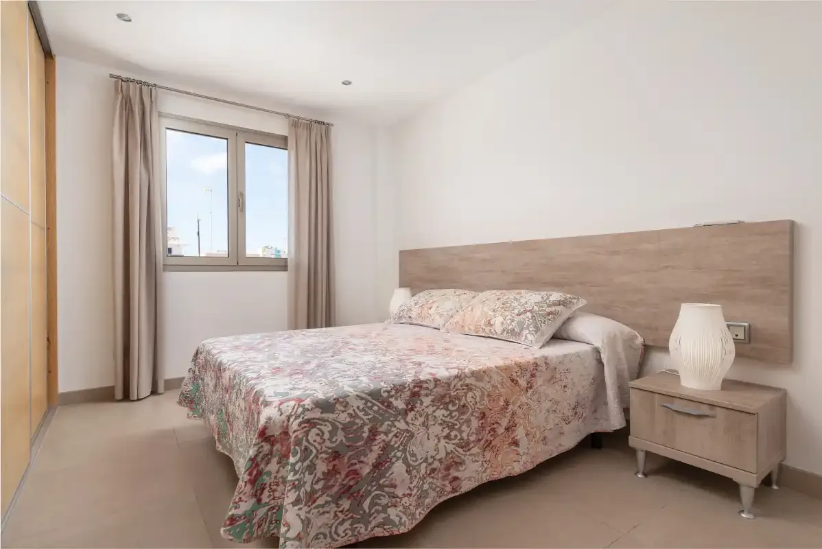A bedroom with a double bed covered by a floral-patterned bedspread.