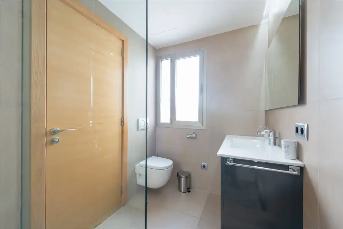 A bathroom with a sink, wall-mounted toilet, and window.