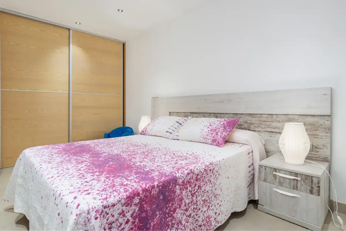 A bedroom with a bed covered in a pink and white floral bedspread.