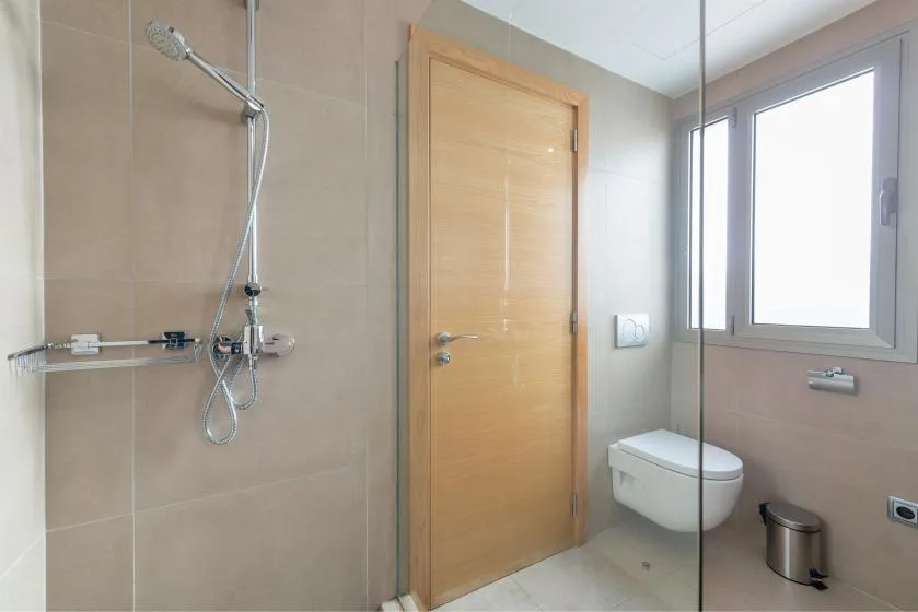 A tiled bathroom with a shower, toilet, and wooden door.