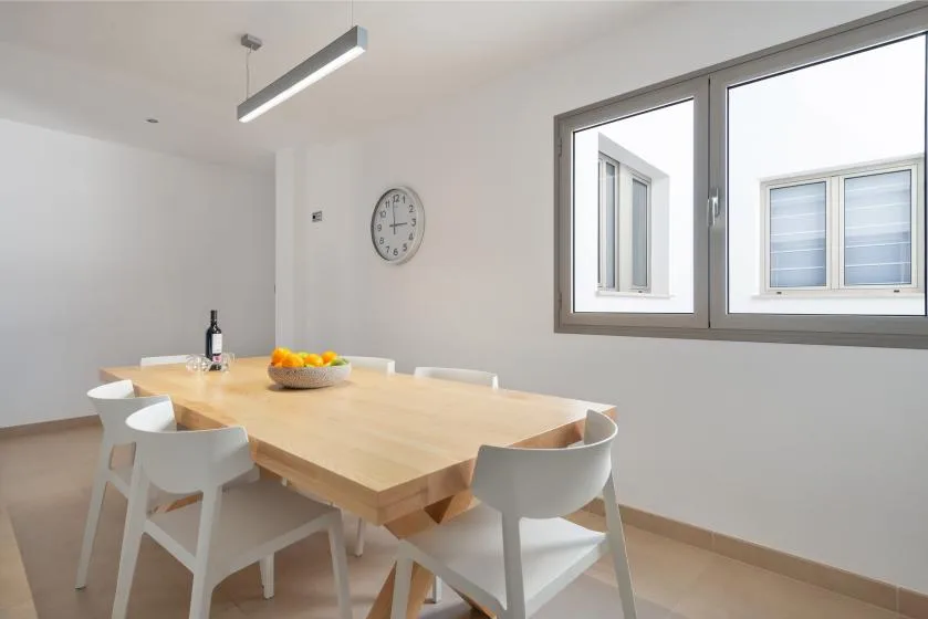 A bright dining area with a long wooden table and several white seats.