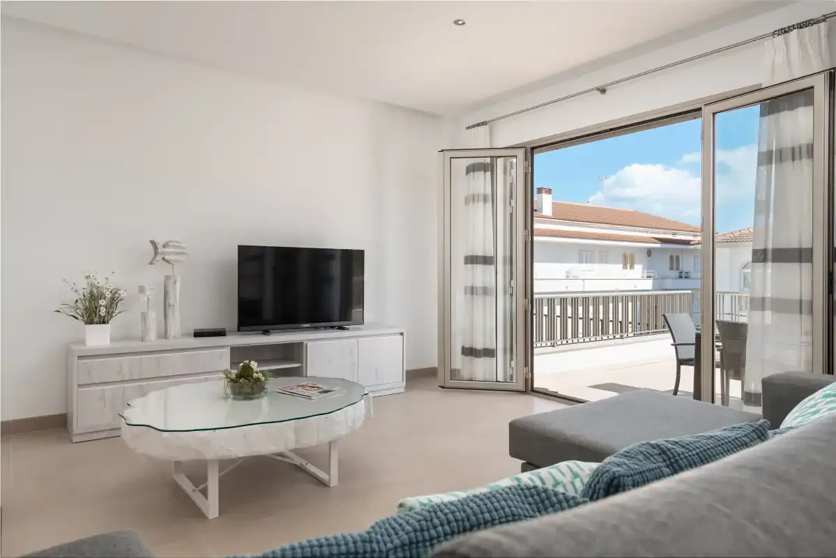 A bright living room opens onto a balcony through wide glass doors.