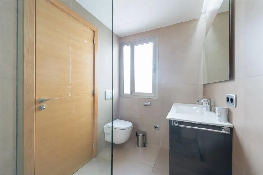 A bathroom with a wall-mounted sink, toilet, and window.