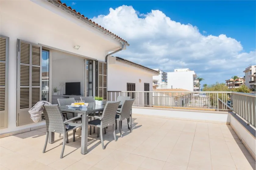 A sunlit terrace has outdoor seating beside a railing and open sky.