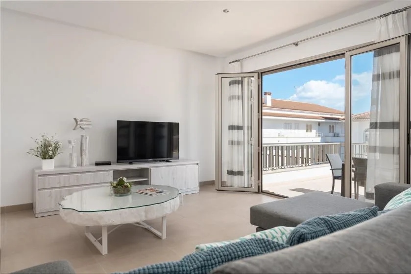 A bright living room opens onto a balcony through wide glass doors.
