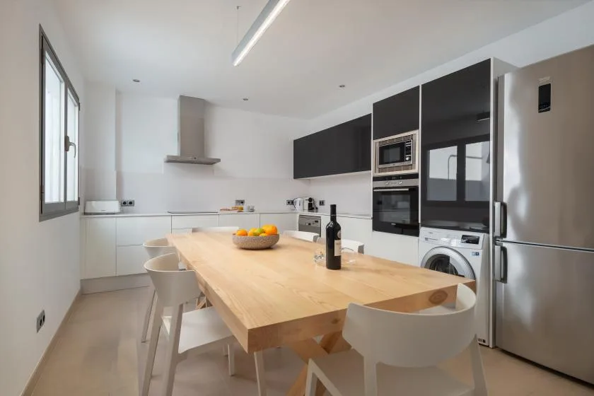 A bright modern kitchen with a wooden dining table and built-in appliances.