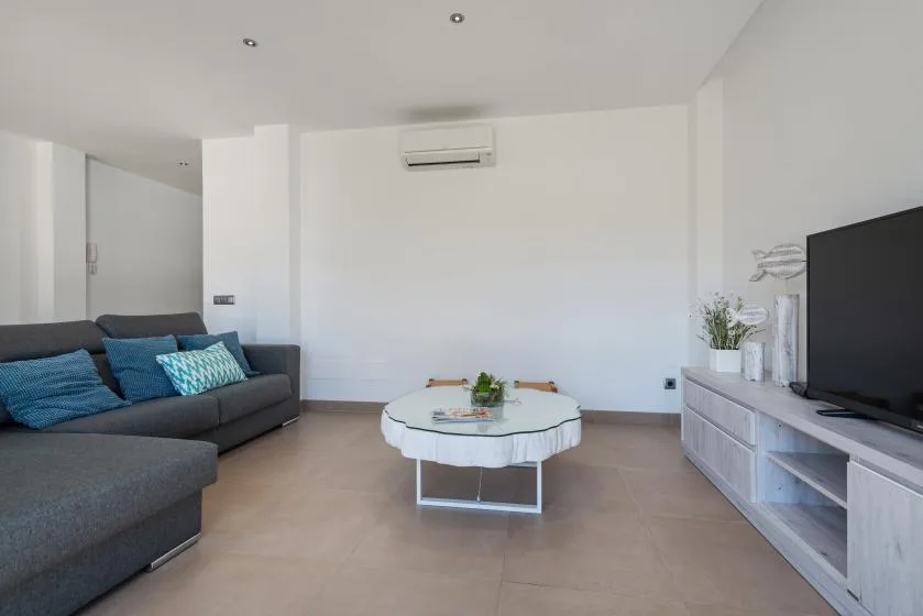 A bright living room with seating, a glass coffee table, and a television.