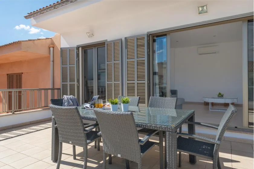 An outdoor dining area with a glass table and woven seating beside open doors.