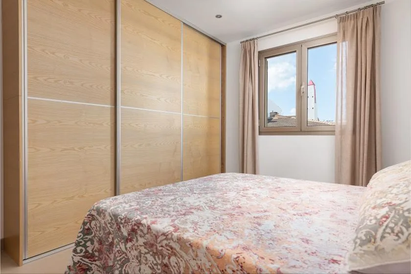A bedroom with a patterned bedspread and a window overlooking a lighthouse.