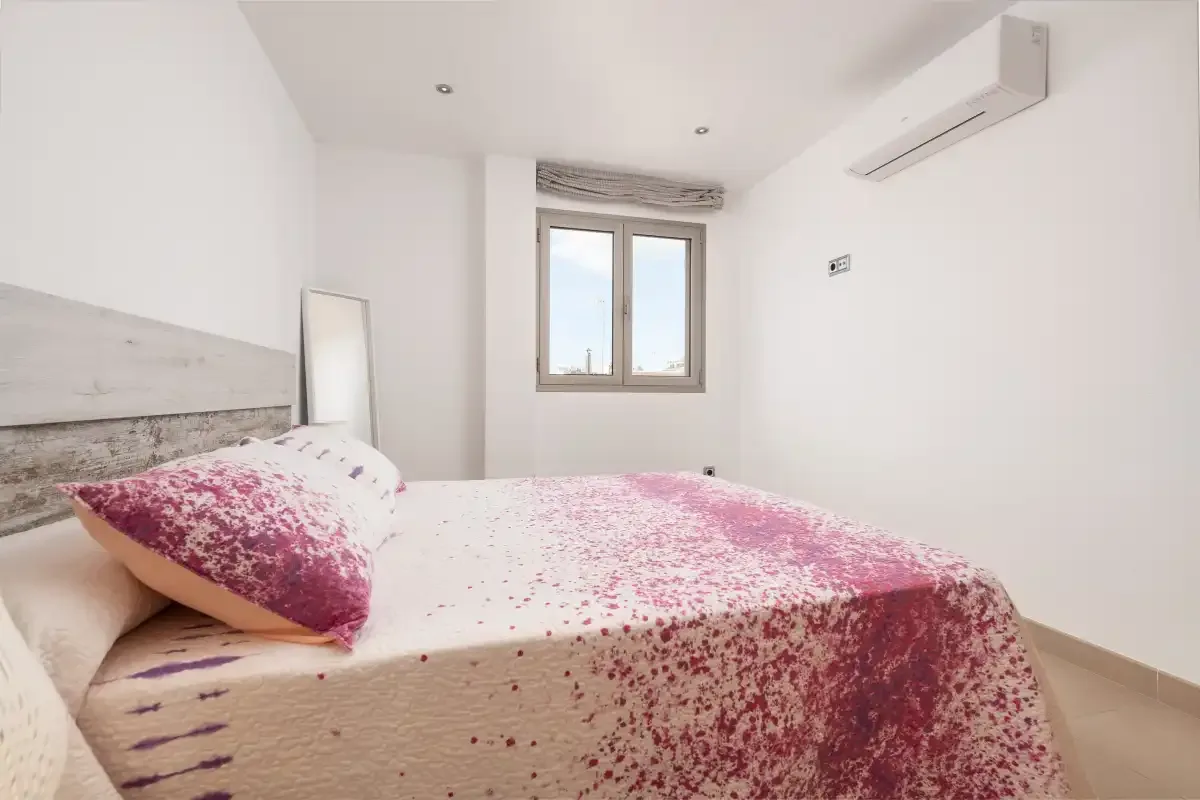 A bedroom with a bed covered in a pink patterned bedspread and a window.
