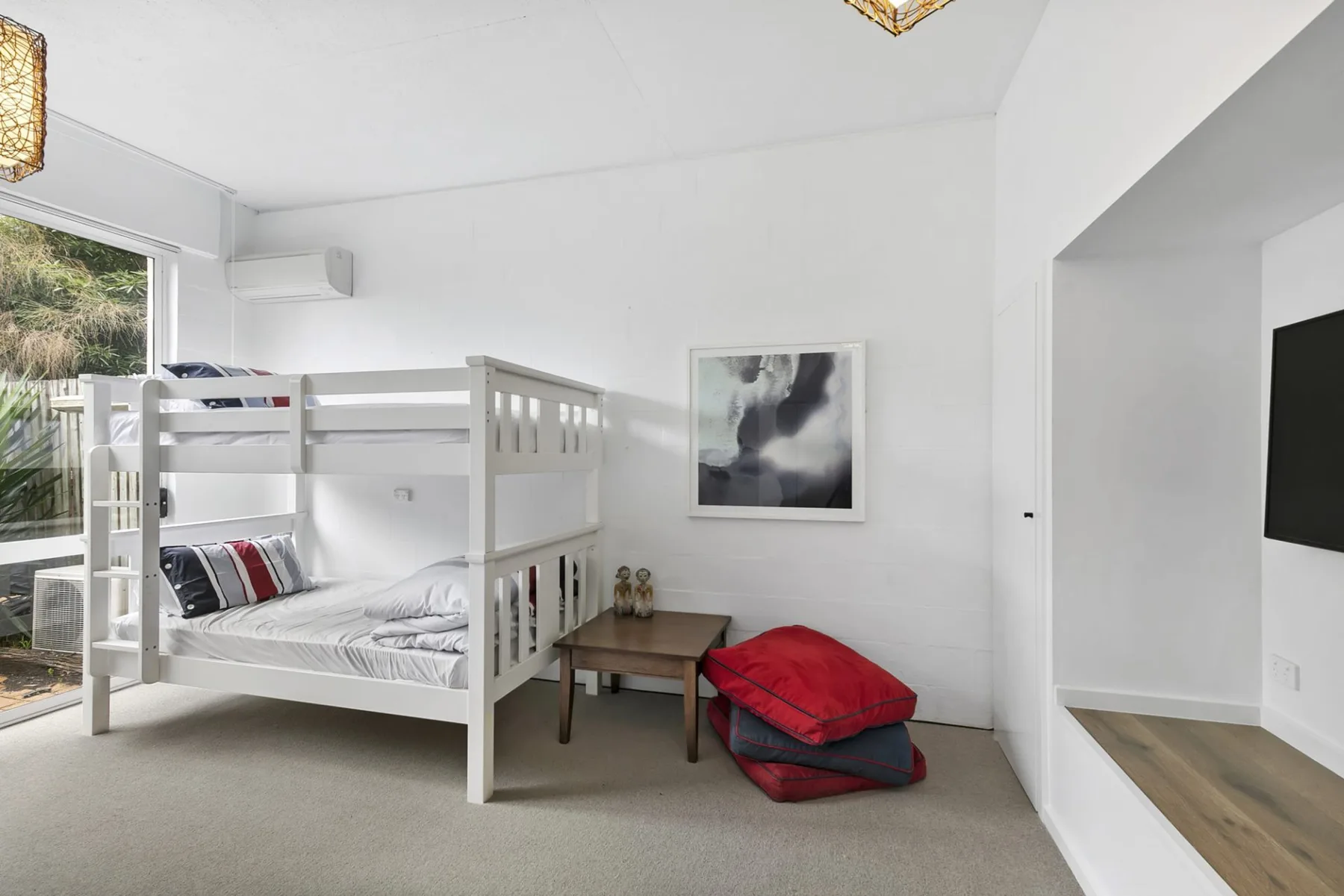 Un dormitorio luminoso con literas y una mesita junto a la ventana.