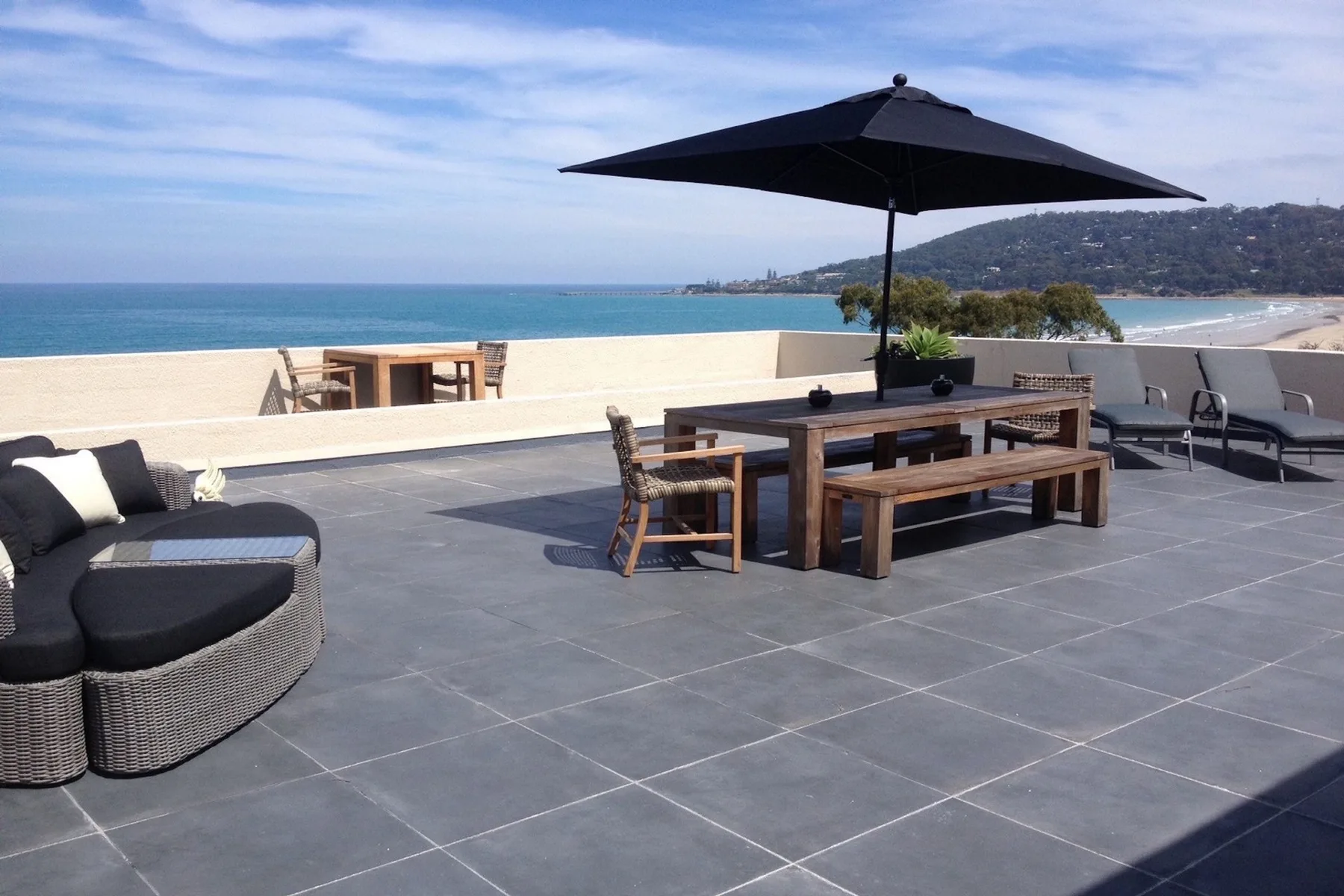 Una terraza junto al mar con asientos al aire libre y una sombrilla grande.