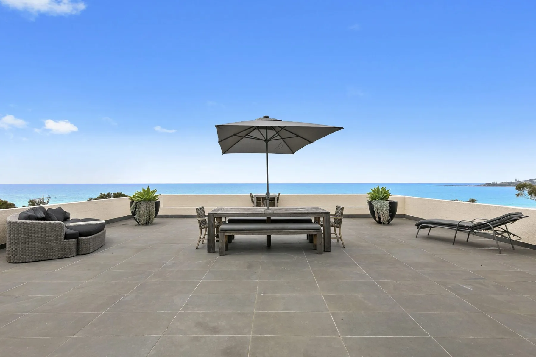 Una terraza junto al mar con asientos al aire libre, una mesa y vistas abiertas al agua.