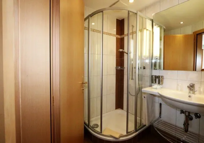Bathroom with glass shower, sink and wood-paneled walls.