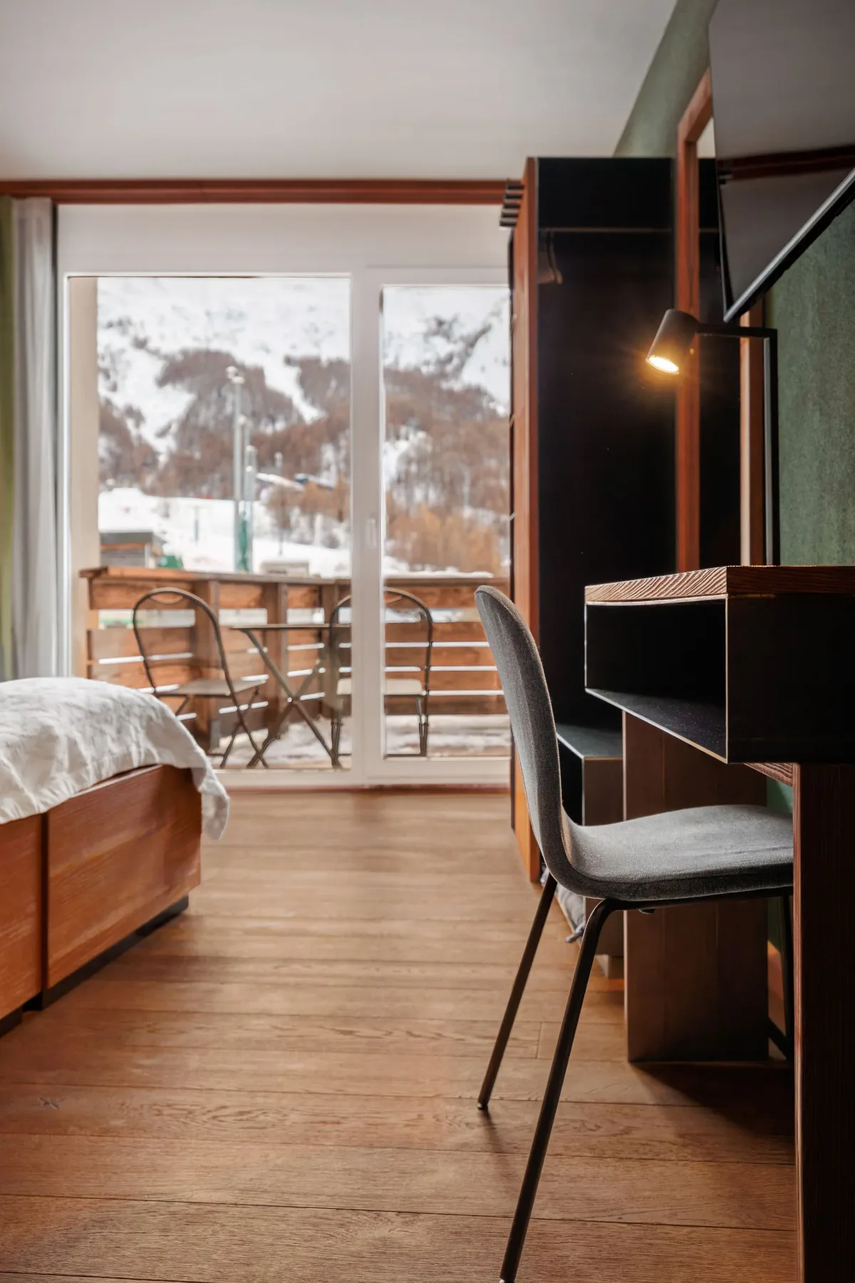 Hotel room with bed, desk chair and balcony.