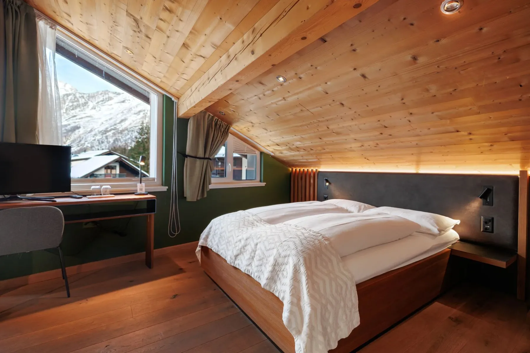 Attic bedroom with sloped wood ceiling, bed and desk.