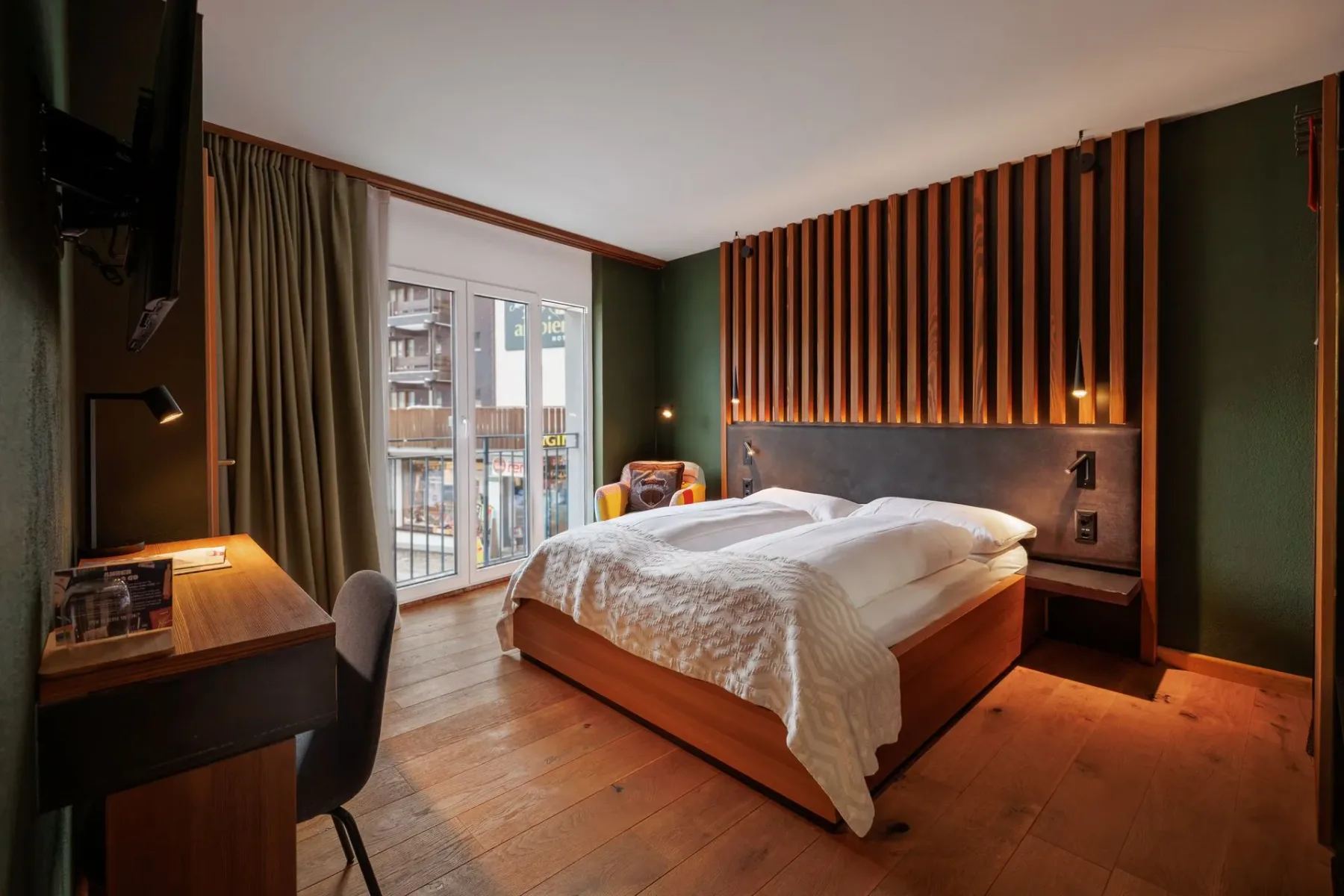 Modern bedroom with a bed, desk and large curtained windows.
