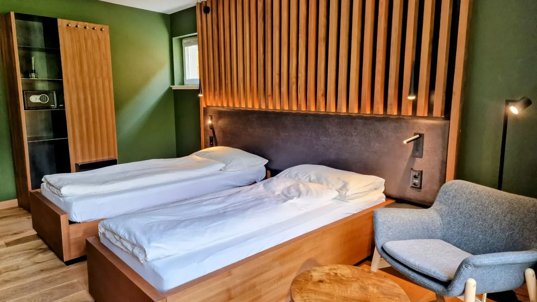 Hotel room with twin beds, wood-slat headboard and armchair.