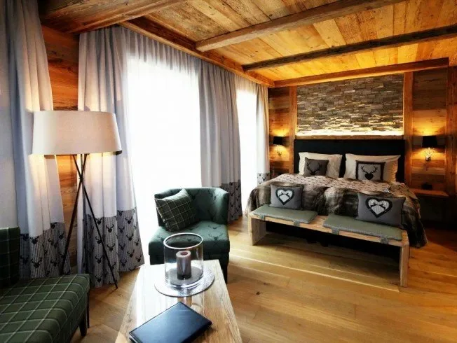 Rustic bedroom with wooden beams, a large bed and an armchair.