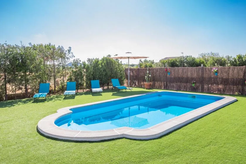 An outdoor swimming pool sits in a grassy yard with lounge chairs nearby.