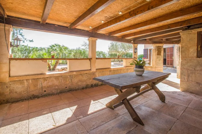A covered patio with a wooden picnic table and open views of greenery.