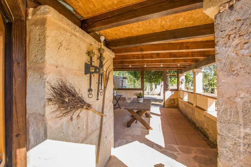 A covered outdoor patio with wooden beams, a table, and surrounding stone walls.