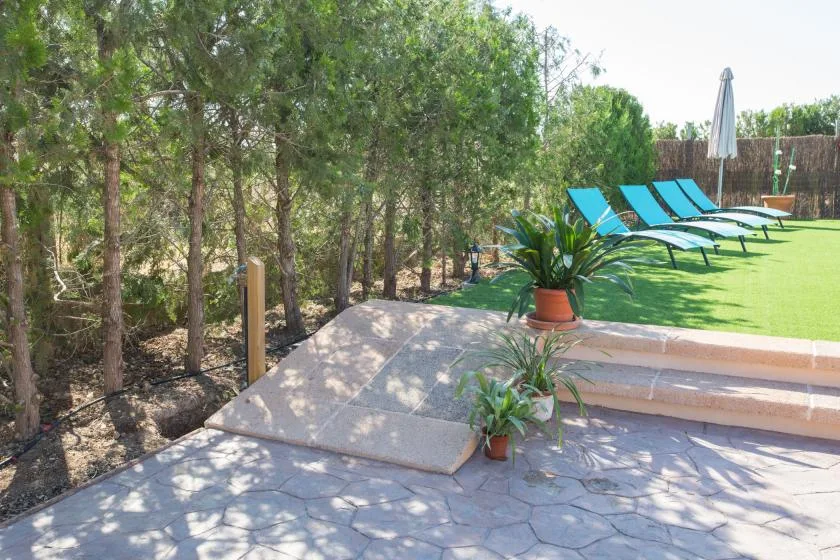A landscaped outdoor patio borders a lawn with lounge chairs and potted plants.