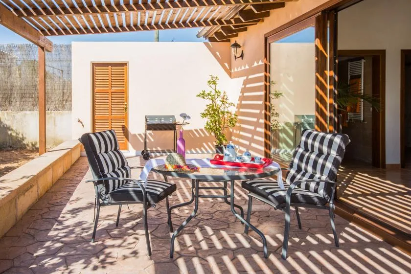 A shaded patio has striped seating around a small table beneath a wooden pergola.