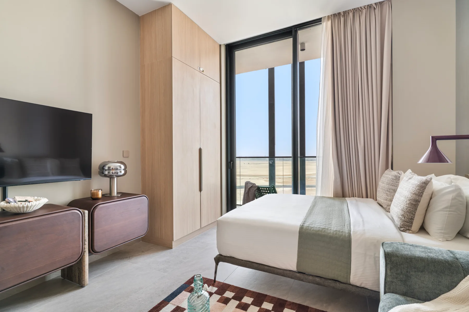 Un dormitorio con una cama bien tendida junto a una gran ventana con cortinas.