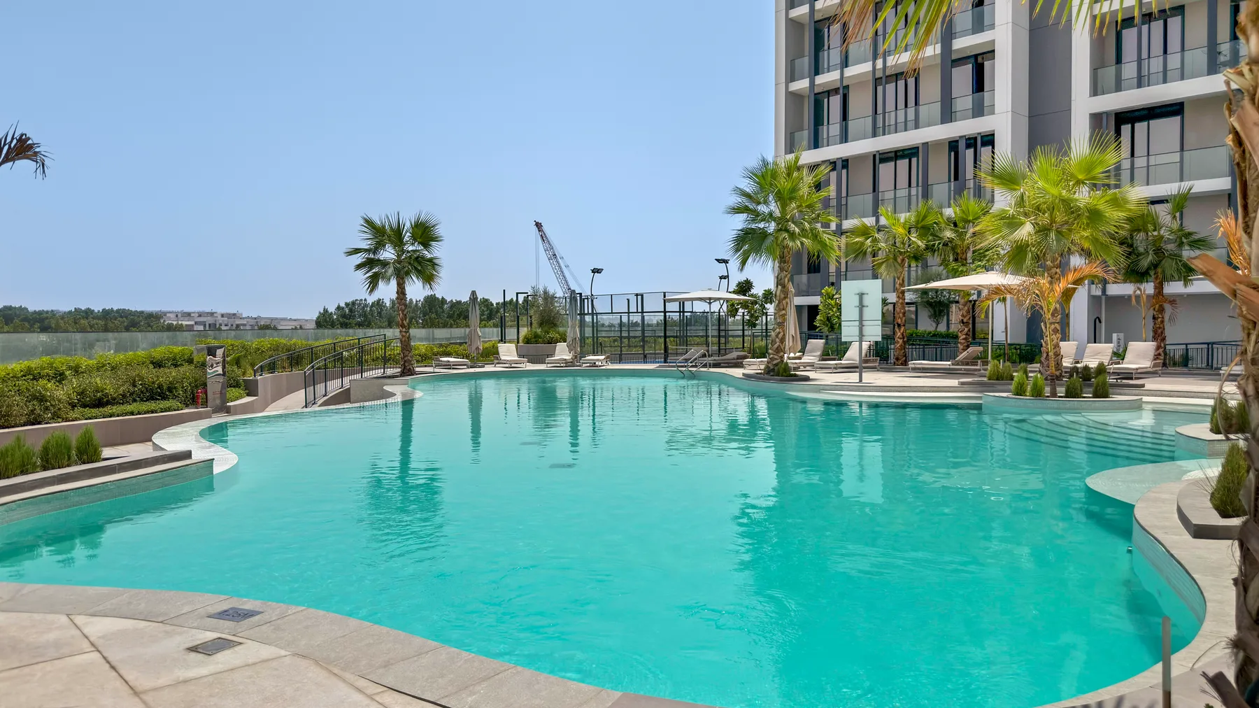 Una amplia piscina al aire libre está junto a un edificio moderno y palmeras.