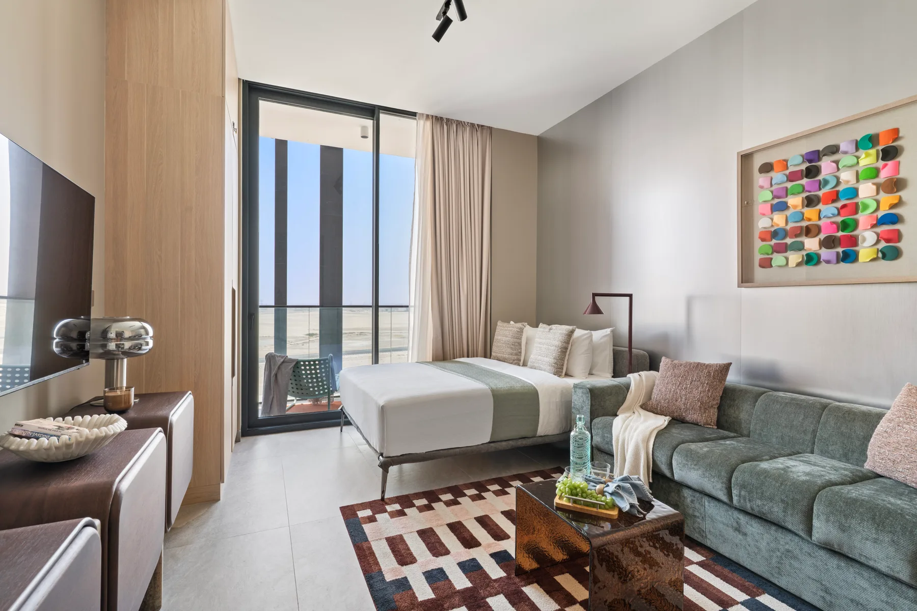 Sala de estar con una cama, un sofá y una puerta de vidrio hacia el balcón.