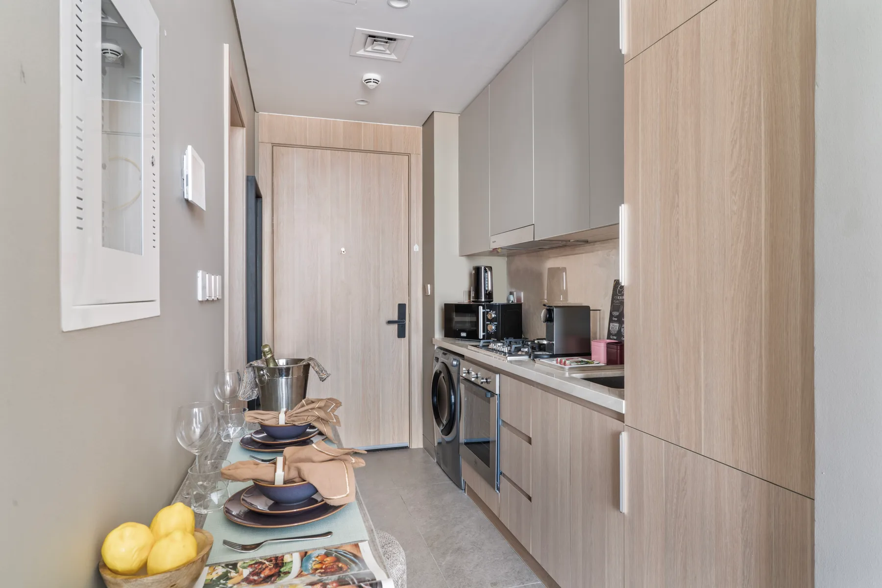 Una cocina estrecha con muebles de madera clara y una mesa puesta junto a la pared.