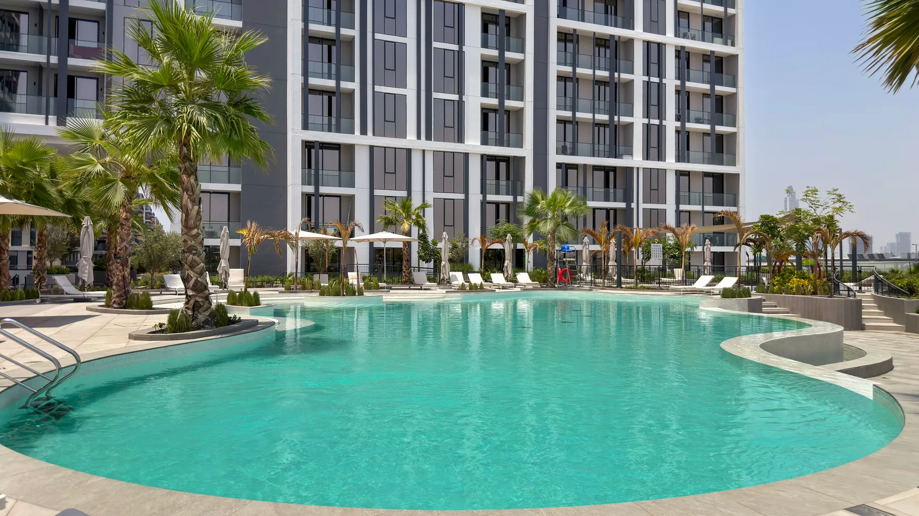 Una gran piscina al aire libre está frente a un edificio moderno con palmeras.