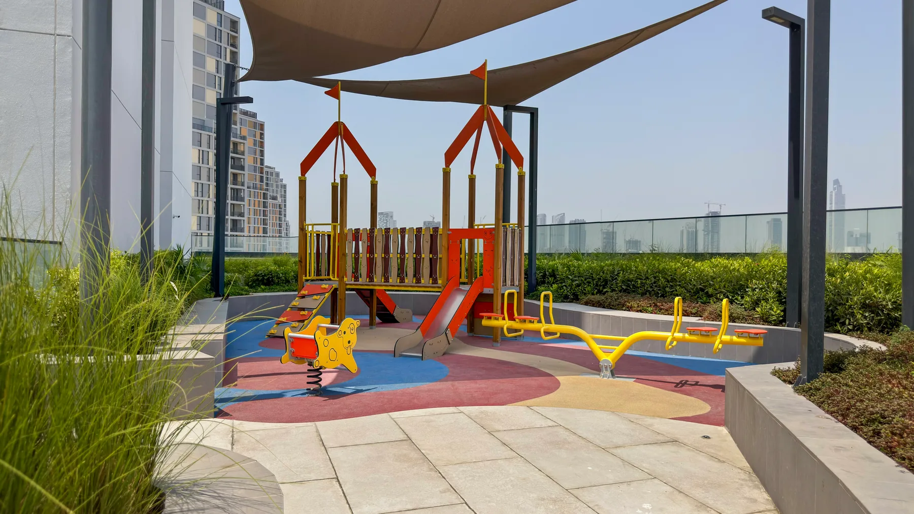 Un parque infantil al aire libre con estructuras de juego coloridas bajo toldos de sombra.