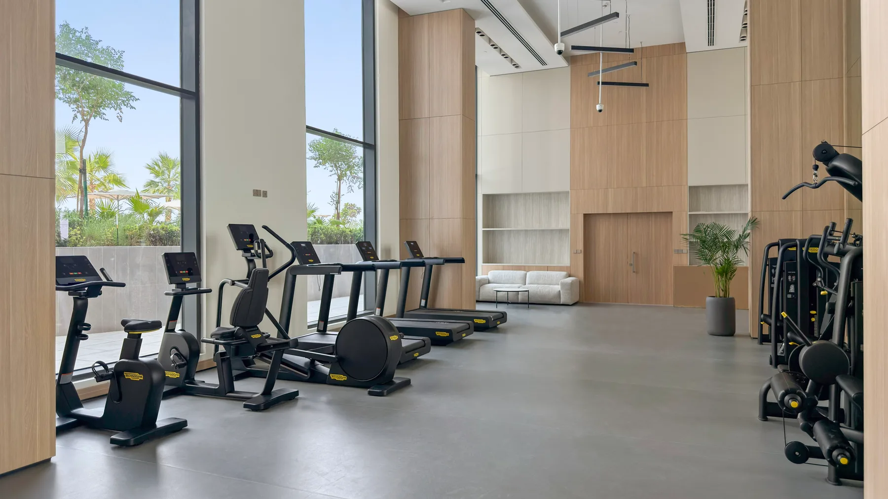 Un gimnasio con equipos cardiovasculares y de fuerza junto a grandes ventanales.